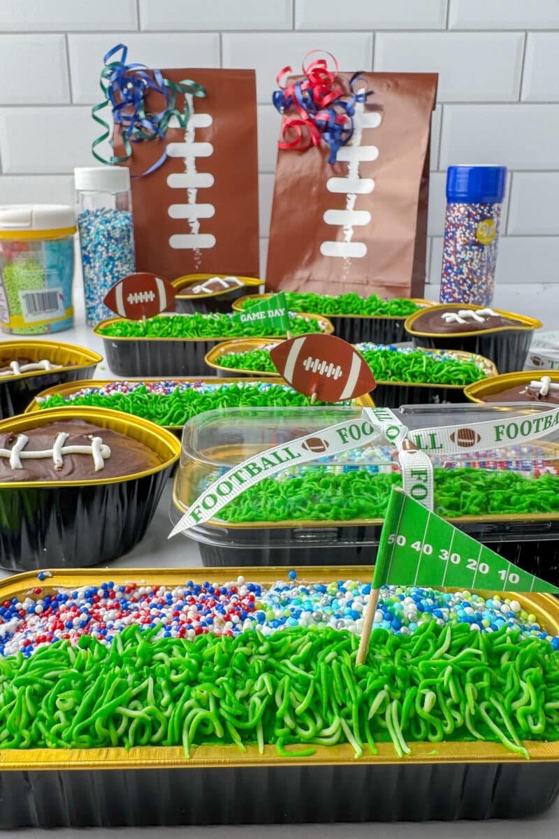 mini loaf pans and football shaped cupcakes on a shite counter with football gift bags and wilton sprinkles in the background