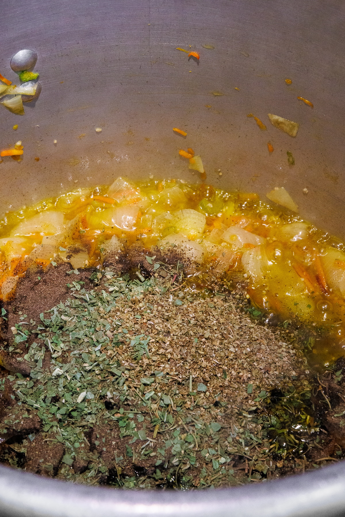 A heap of dried oregano, basil, and black pepper added to the vegetable base.