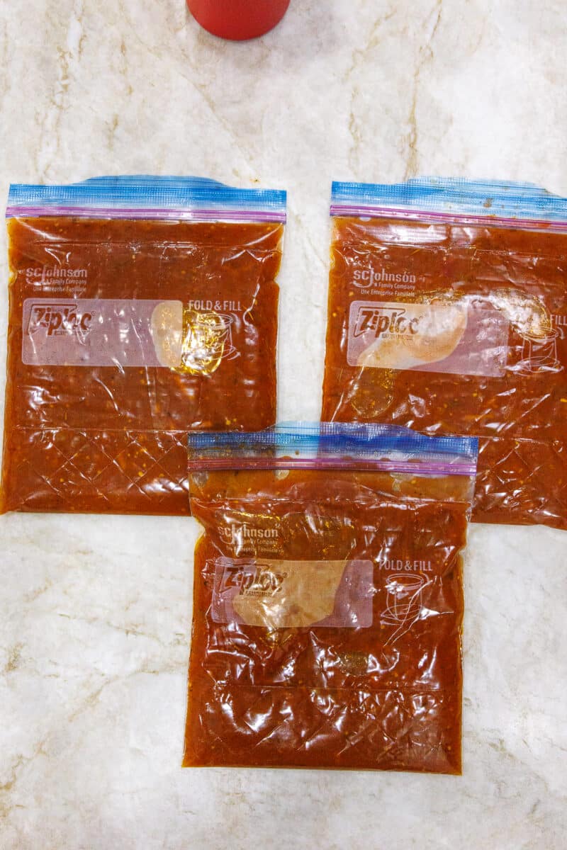 Three Ziploc bags filled with tomato sauce laid flat on a marble countertop for space-saving.