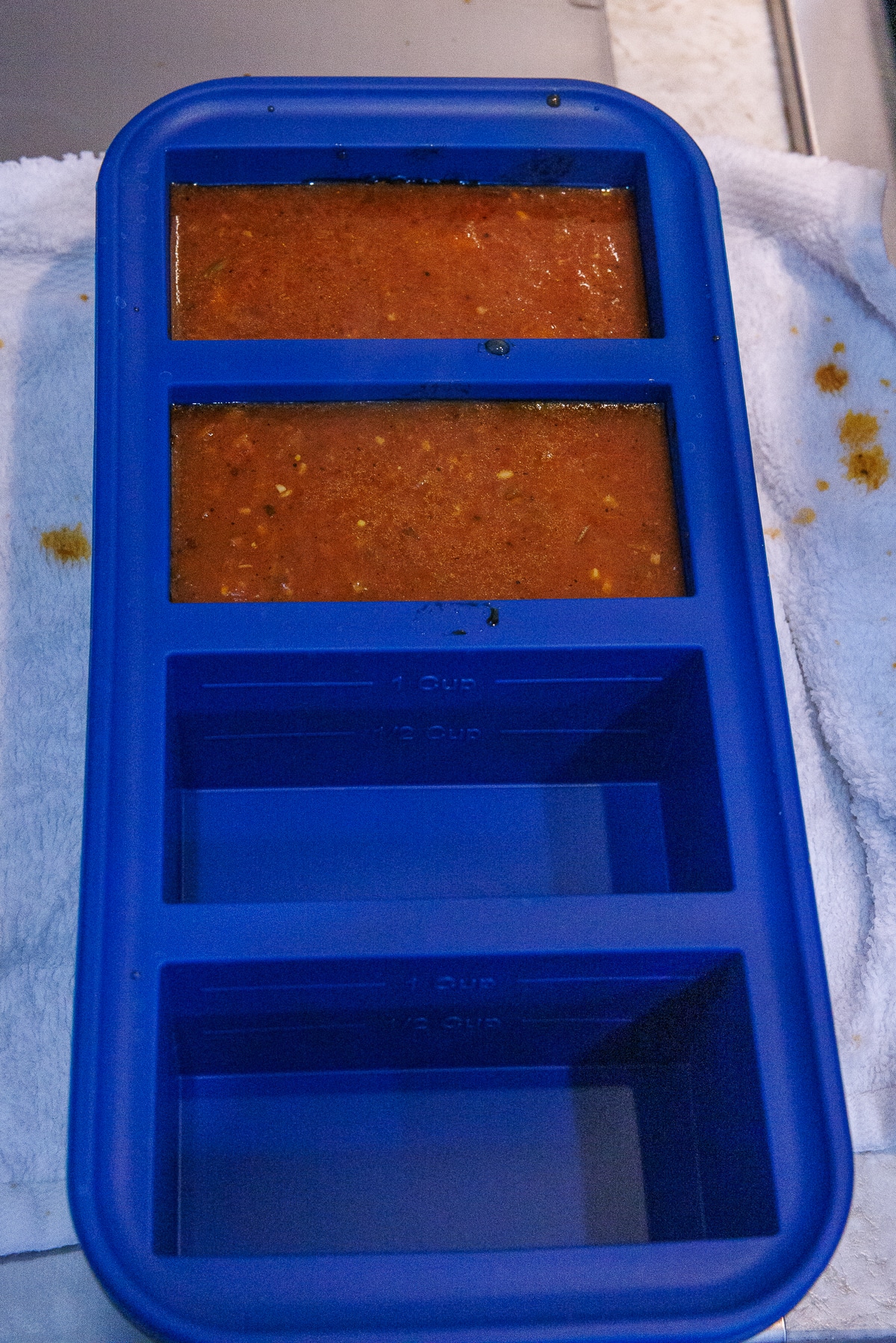 A blue silicone Souper Cubes tray partially filled with 1-cup portions of tomato sauce.