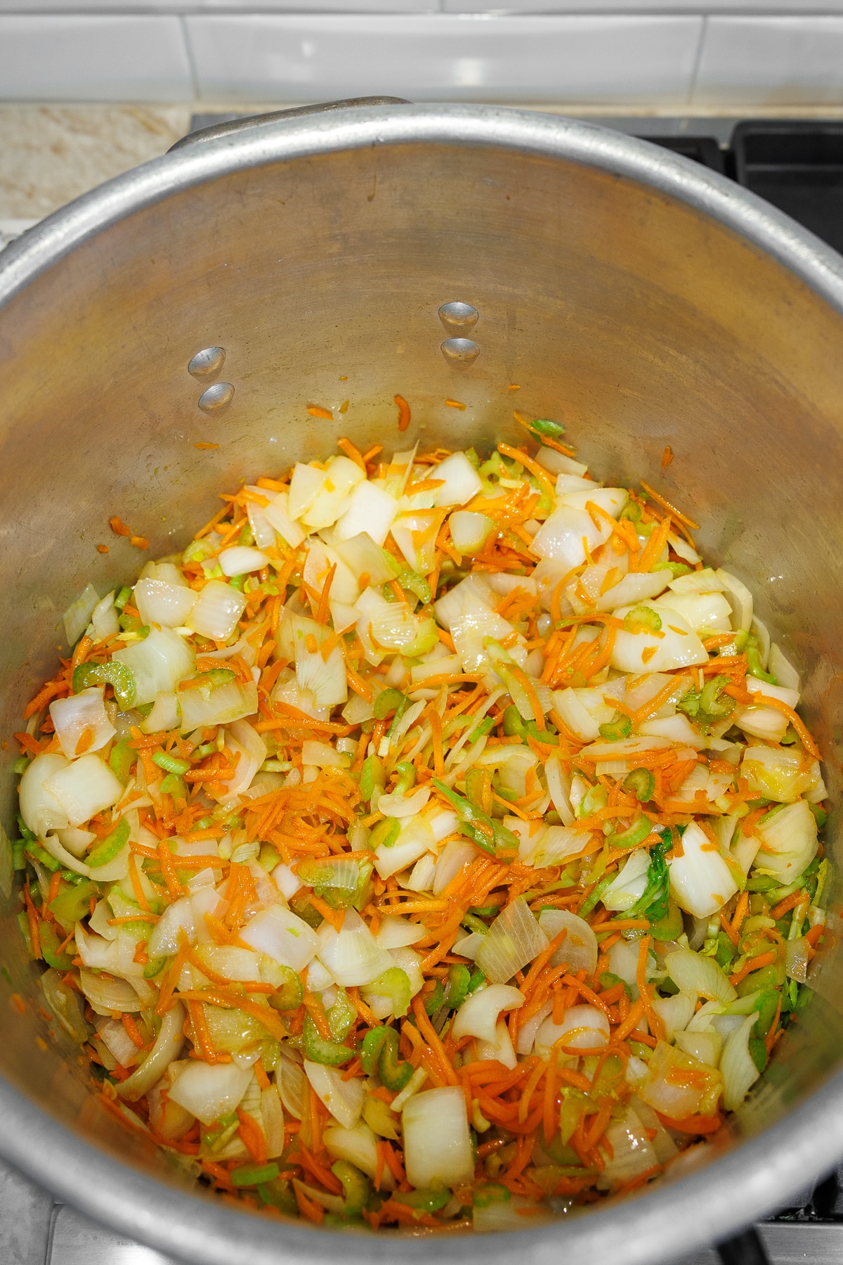 Freshly chopped onions, shredded carrots, and sliced celery mixed together in a pot.