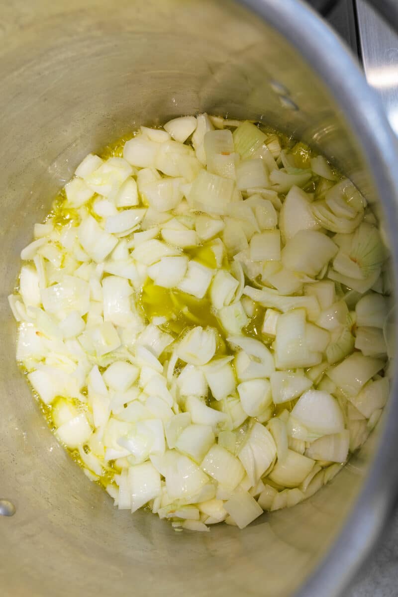 Diced white onions simmering in a pool of golden olive oil in a large stockpot.