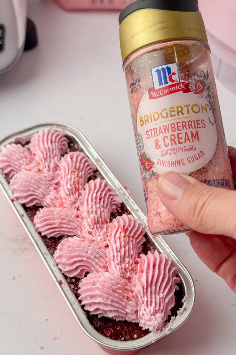 Close up of McCormick Bridgerton Strawberries and Cream sugar being held over a freshly frosted chocolate mini loaf.