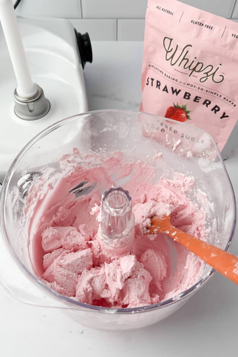 Finished batch of smooth, pink strawberry buttercream in a mixer bowl with a spatula.