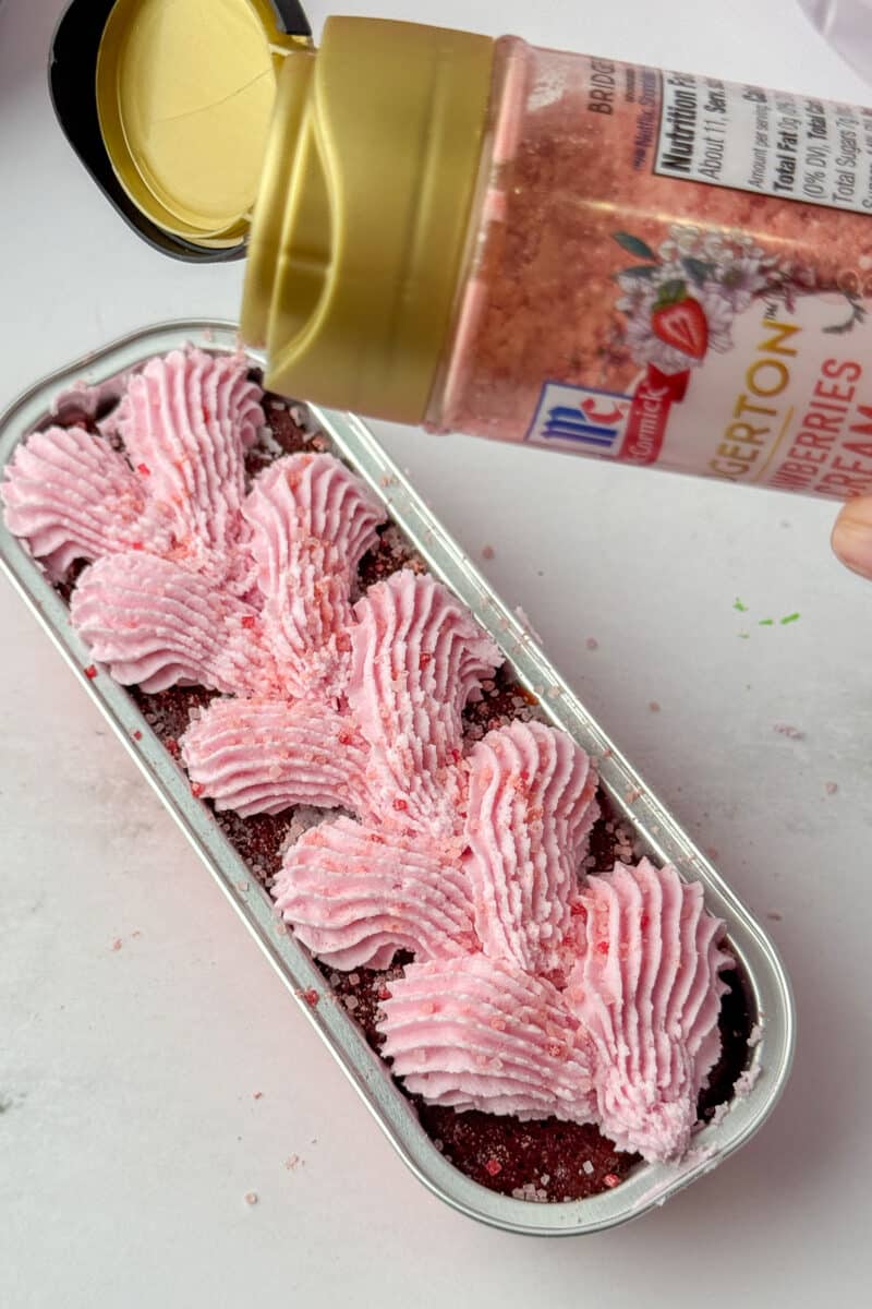 Sprinkling McCormick Bridgerton Strawberries & Cream sugar over piped strawberry frosting on a mini loaf.