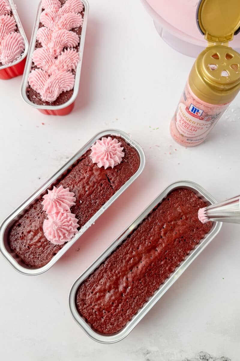 Piping pink strawberry buttercream stars onto chocolate mini dessert loaves in silver tins.