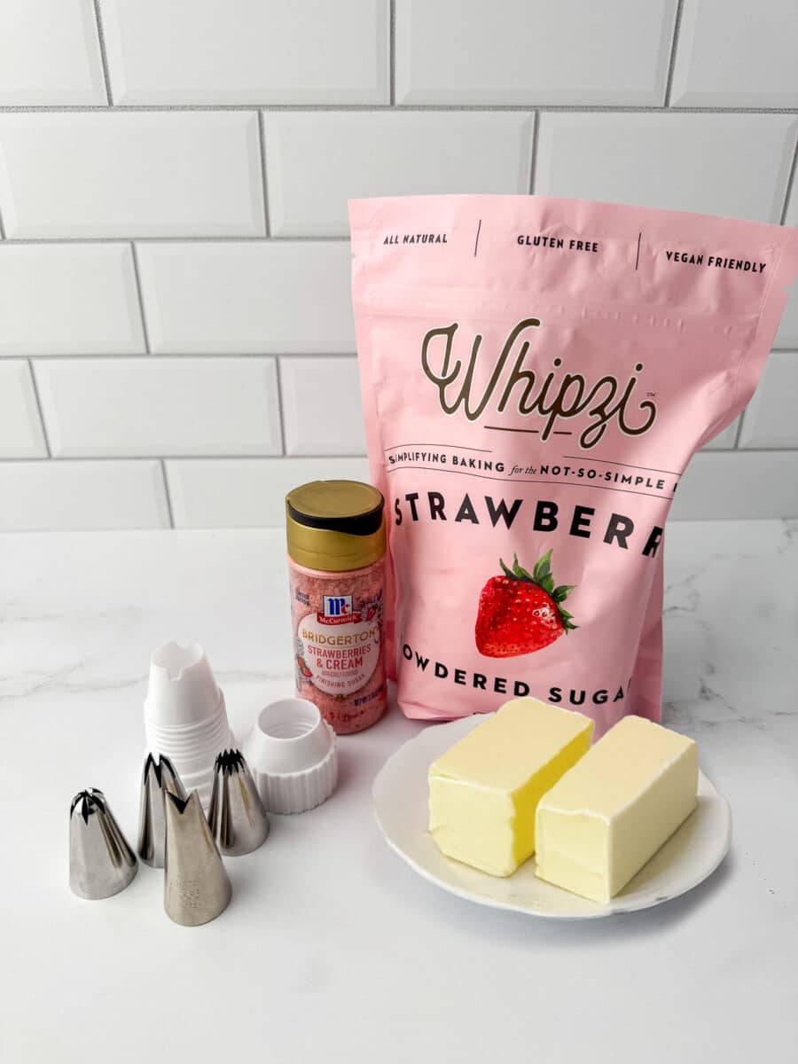 Ingredients for strawberry buttercream including two sticks of butter, pink Whipzi powdered sugar, and piping tips.