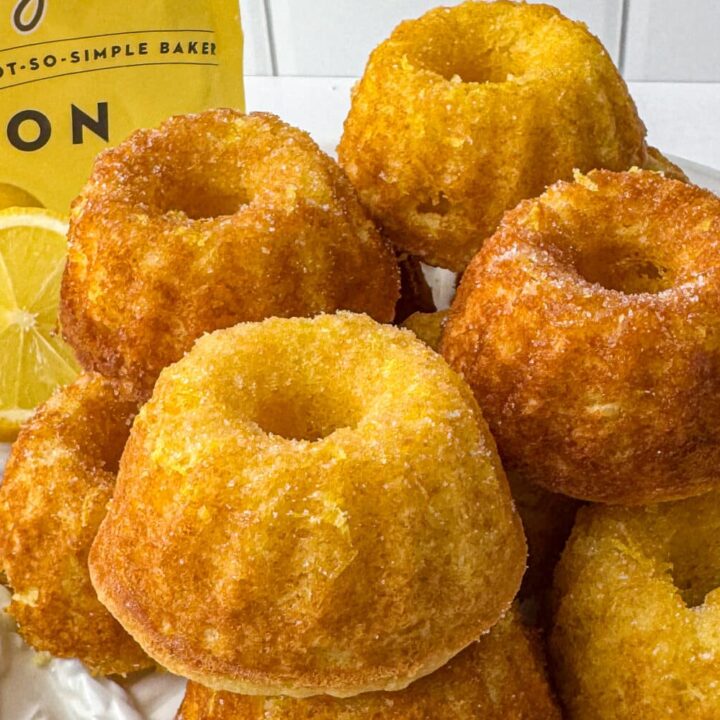 A vibrant stack of homemade mini lemon drizzle cakes on a white plate, perfect for a bright citrus dessert presentation.