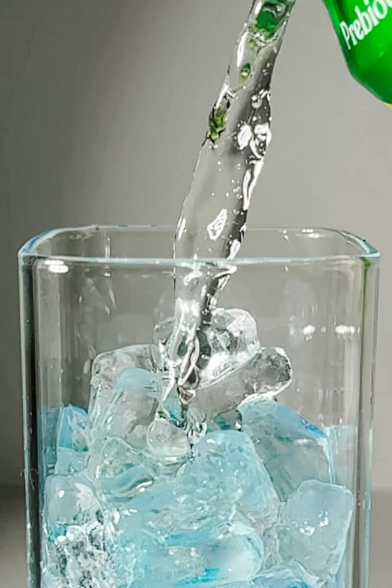 Pouring Lemon Lime Poppi prebiotic soda into a glass with blue raspberry syrup and ice.