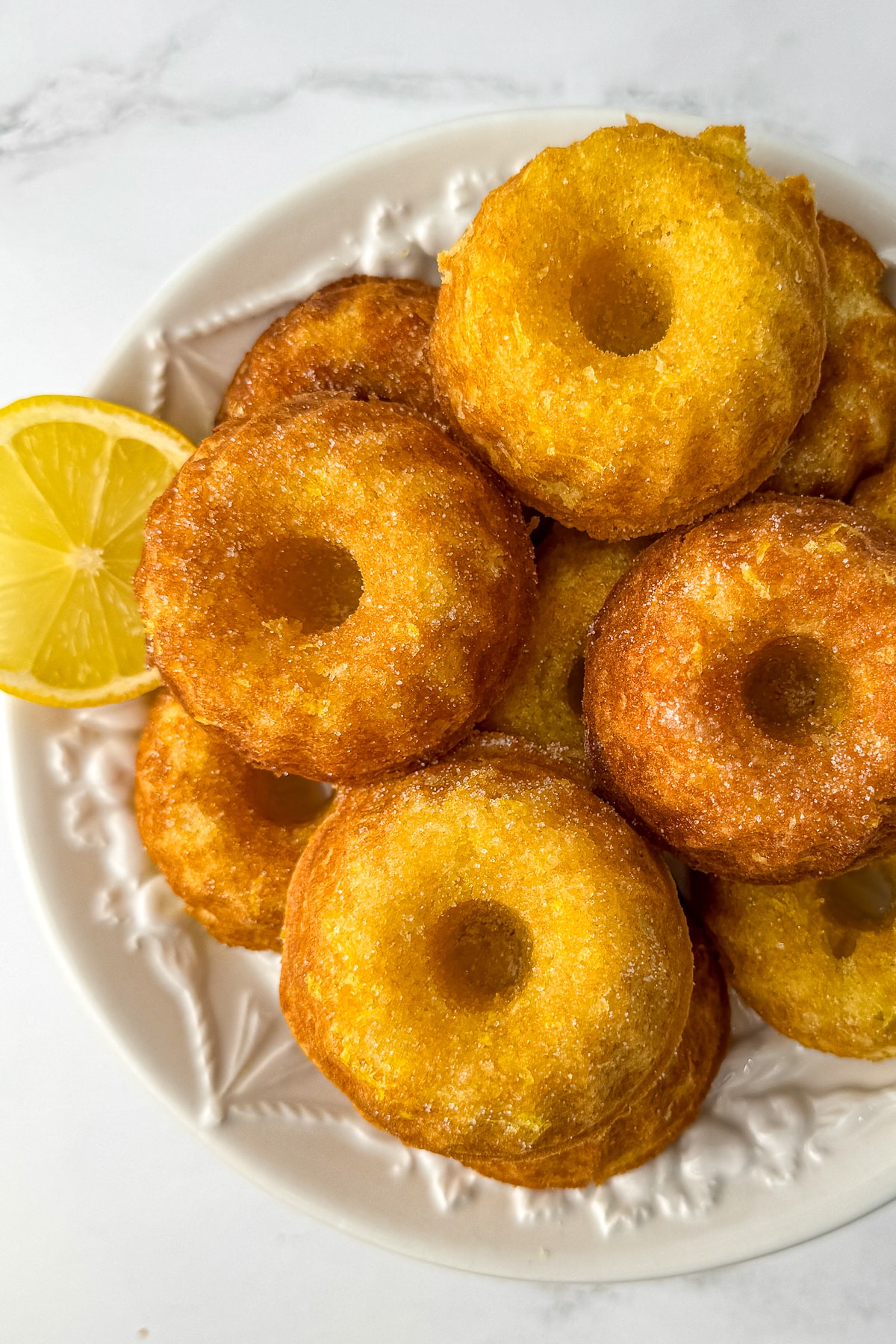 Overhead view of a plate filled with golden-brown mini lemon drizzle cakes, showcasing the classic bundt shape and lemon garnish.