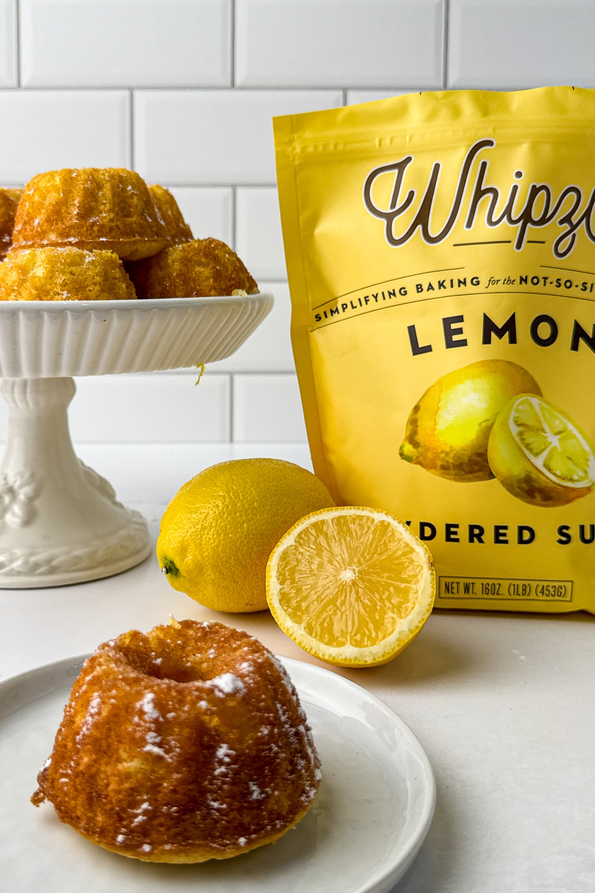 A display of mini lemon drizzle cakes with Whipzi sugar and fresh lemons on a bright kitchen counter.