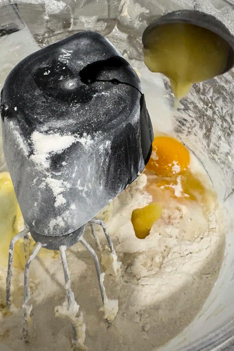 Close-up of fresh eggs and liquid ingredients being poured into the bowl for the best mini lemon drizzle cakes recipe.