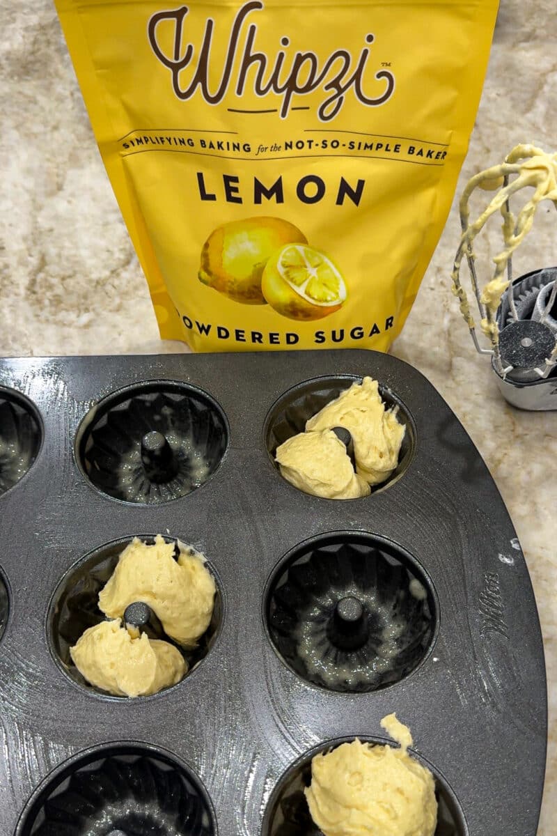 A bag of Whipzi lemon powdered sugar in the background as mini bundt cake pans are filled with lemon cake batter.