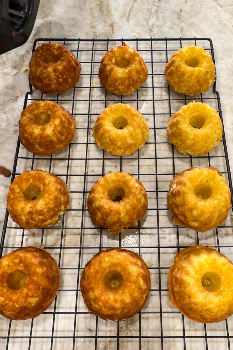 A wire cooling rack filled with freshly baked, golden-brown mini bundt cakes ready for the lemon drizzle topping.