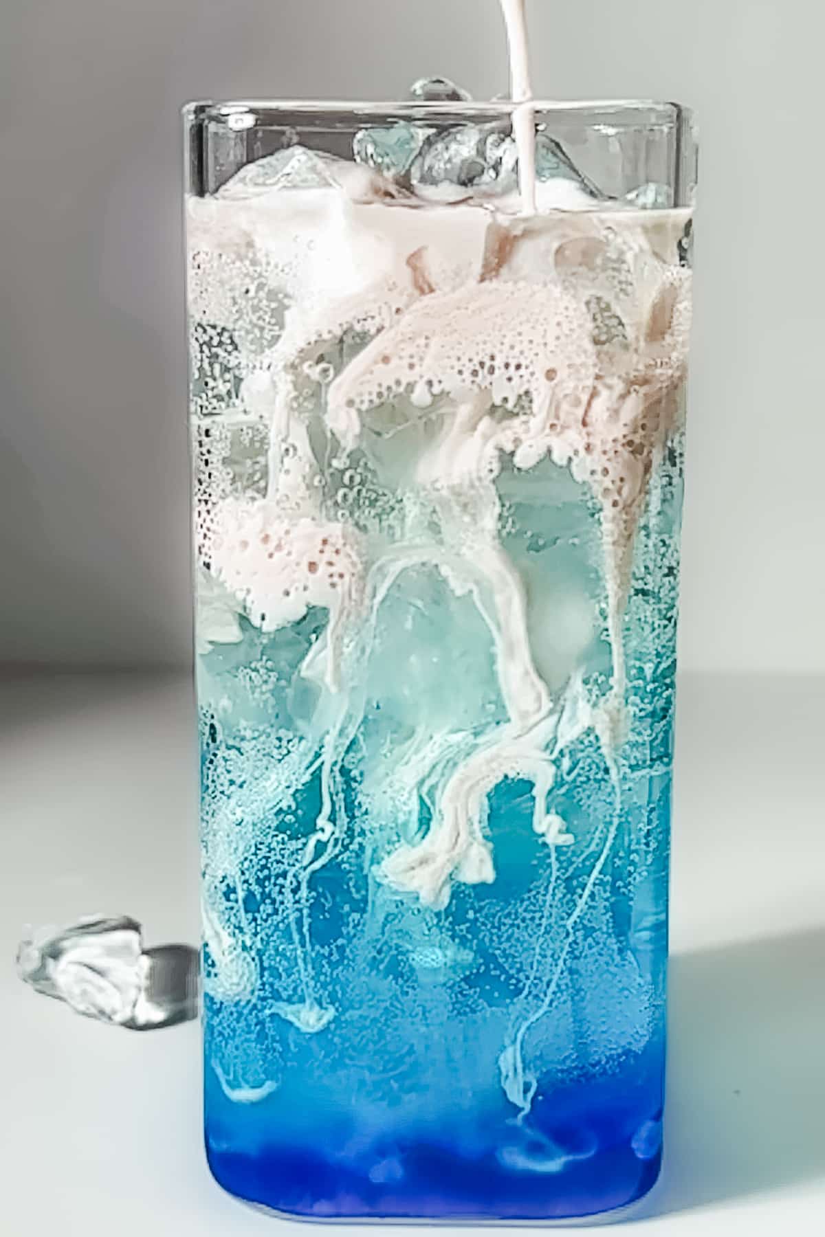 Pouring frothed strawberry cream over a blue Poppi soda to create a "dirty" swirling effect.