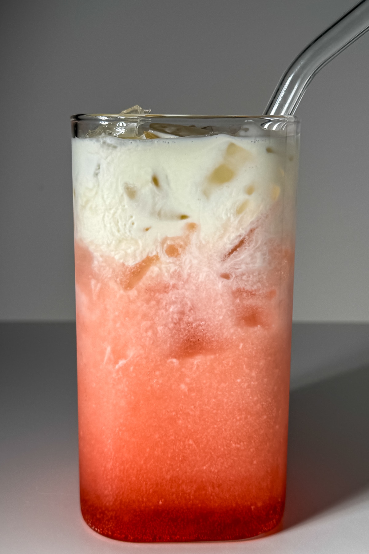 A layered raspberry vanilla lemon-lime dirty soda in a clear glass with ice, showing a bright pink carbonated gradient and a thick, velvety white heavy cream float cascading down from the top.