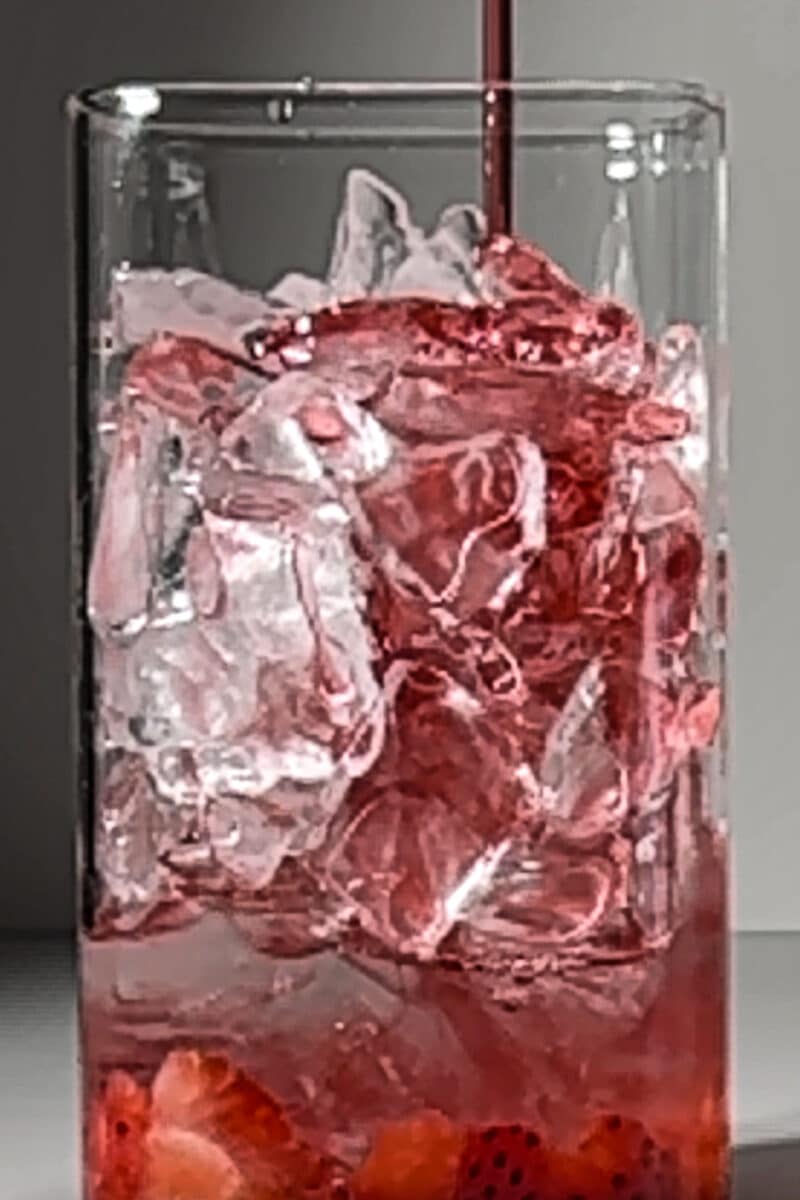 The beautiful layered effect of red strawberry syrup and golden Poppi soda in a tall glass.