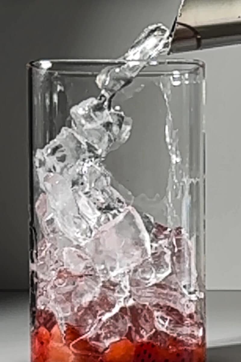Clear glass filled with fresh strawberries and topped with pebble ice for a cold drink.