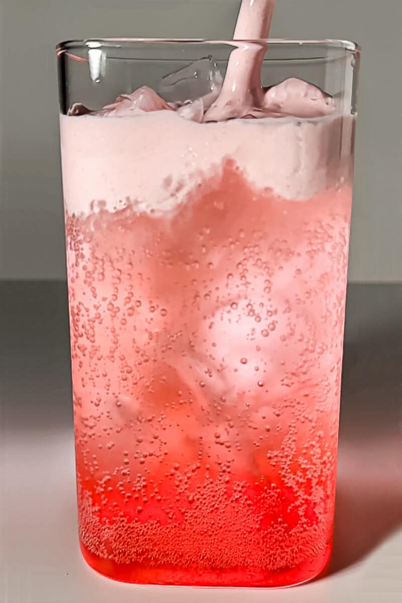 A layered strawberry peach lemon-lime dirty soda in a tall clear glass with ice, bright pink carbonated bubbles, and a thick layer of homemade pink strawberry cold foam on top.