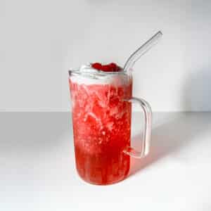 A bright red, bubbly Vanilla Shirley Temple dirty soda mug filled with ice and topped with thick white canned cold foam and maraschino cherries